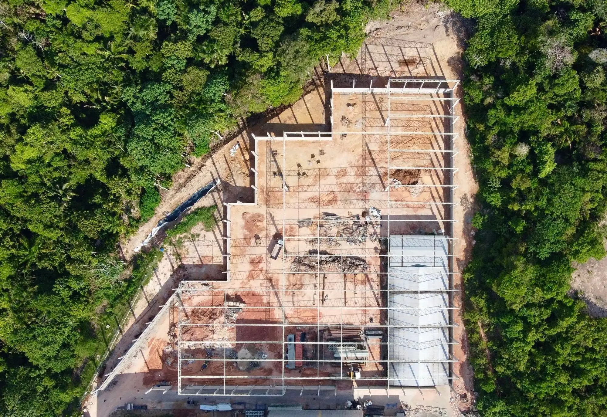 Vista aérea, de cima, do galpão industrial em obra no meio da mata, com a estrutura metálica montada