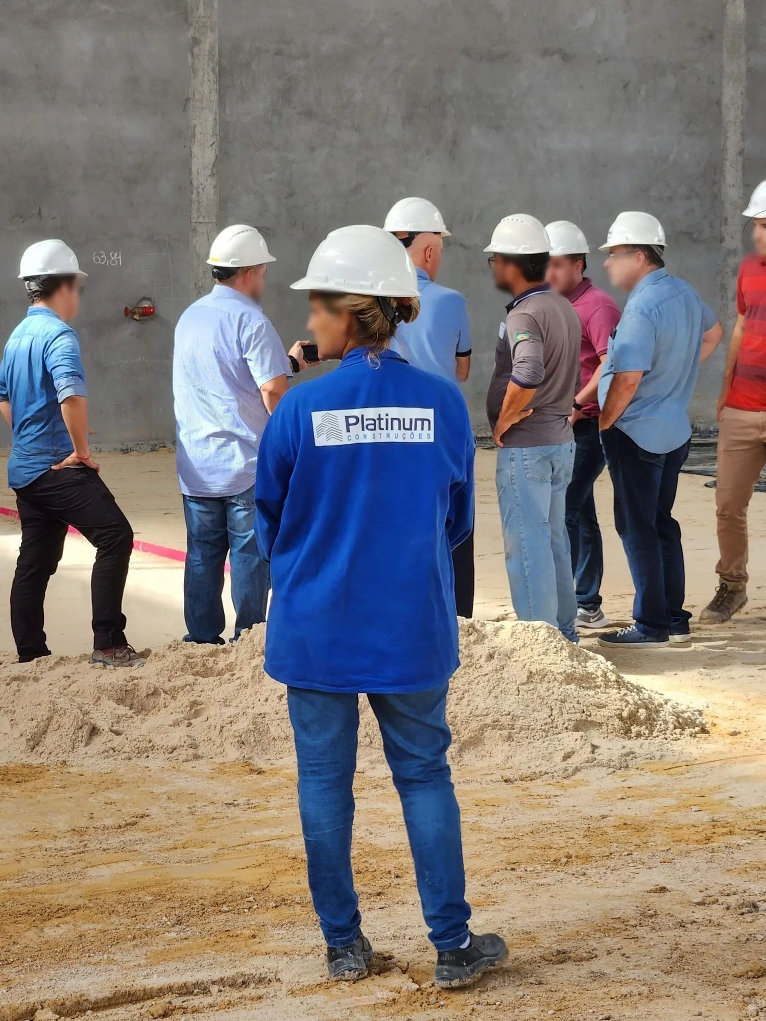 Equipe de capacete reunida no canteiro, em pé diante de uma parede de concreto